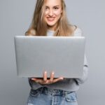 Free Photo _ Young happy smiling woman in casual clothes holding laptop and sending email to her best friend isolated on gray background