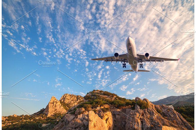 Big white airplane is flying over rocks at sunrise