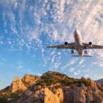 Big white airplane is flying over rocks at sunrise